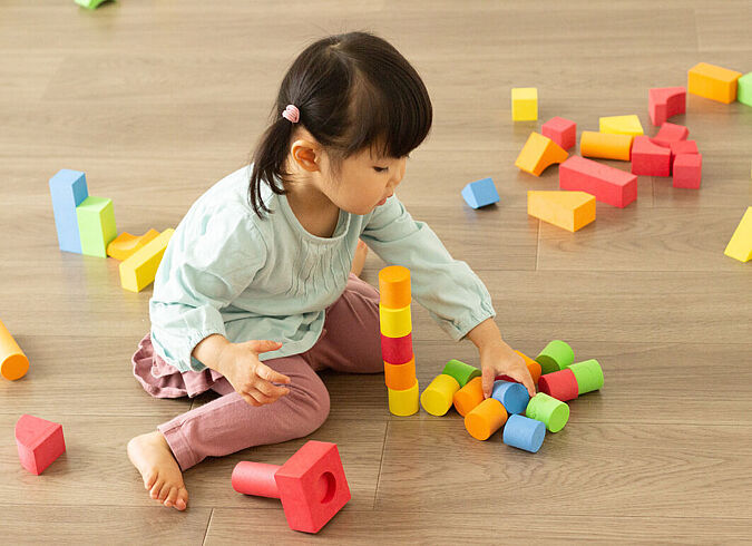 Ein Kleinkind spielt mit bunten Bauklötzen auf dem Boden.