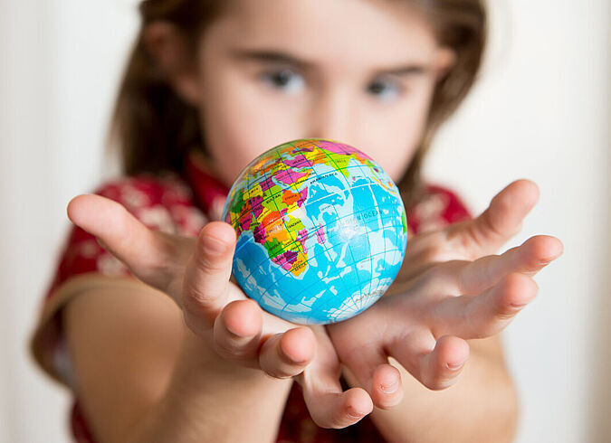 Ein Kind hält eine kleine Weltkugel in ihren offenen Handflächen