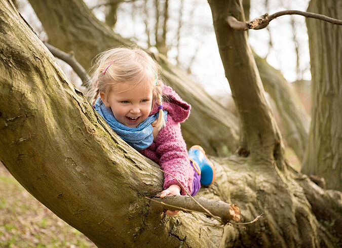 Ein Kind klettert einen Baumstamm entlang und lacht dabei.