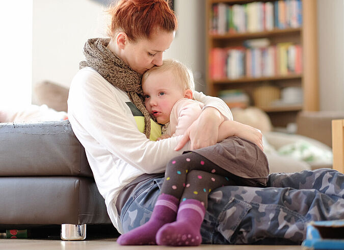 Eine Mutter hält liebevoll ihr erkranktes Kind sitzend auf dem Schoß.