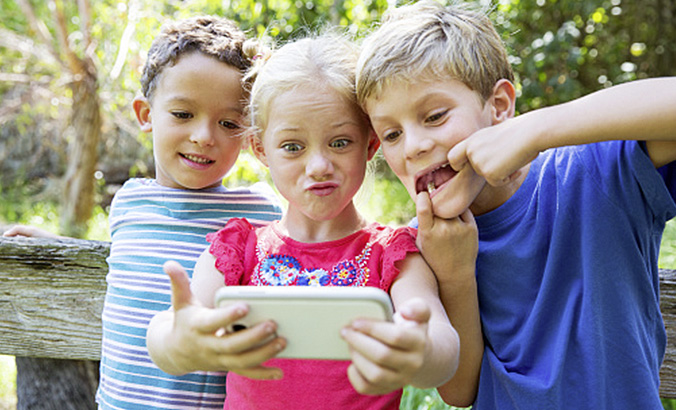 Drei Kinder fotografieren sich mit einem Smartphone