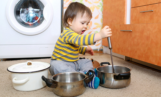 Kind sitzt auf dem Küchenboden und spielt mit Töpfen