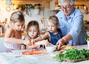 Ältere Frau belegt mit drei Kindern eine selbstgemachte Pizza