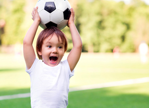 Kind hält sich einen Fußball über den Kopf