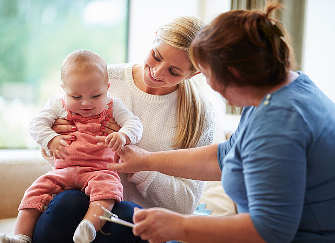 Eine Oma bestaunt das Baby ihrer Tochter, das auf dem Knie der Mutter sitzt.