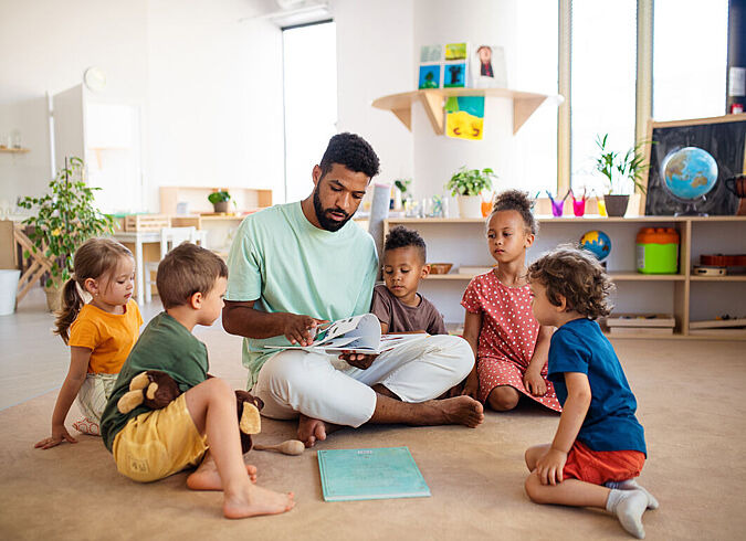 Ein Erzieher liest den Kindern im Kindergarten eine Geschichte vor.