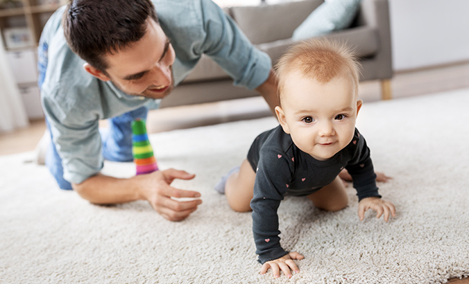 Vater begleitet krabbelndes Baby auf dem Wohnzimmer-Teppich