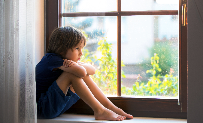 Kind schaut traurig aus dem Fenster