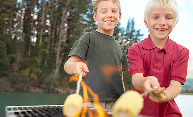 Zwei Jungen grillen Maiskolben