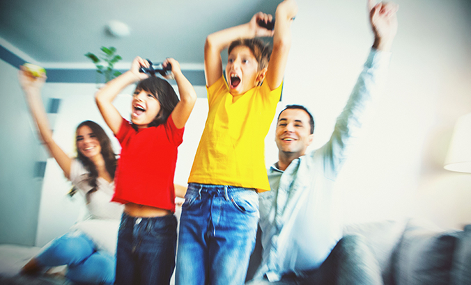 Familie spielt gemeinsam mit Spielekonsole und jubelt