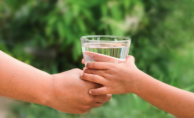 Kinderhand greift nach Wasserglas, welches von einer erwachsenen Hand gereicht wird
