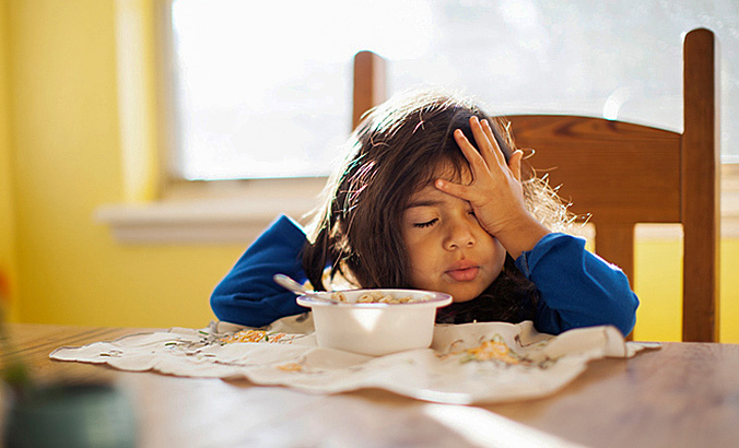 Kind sitzt müde am Frühstückstisch