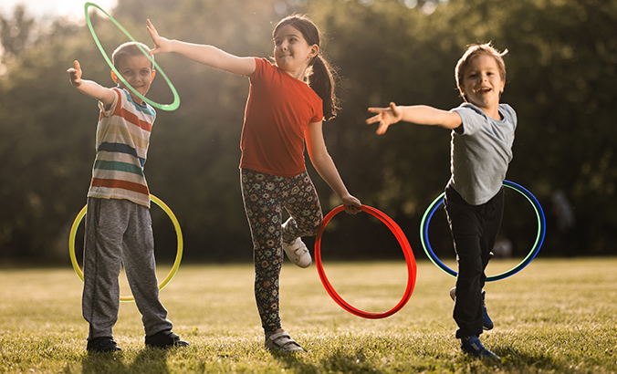 Drei Kinder spielen mit bunten Reifen auf einer Wiese