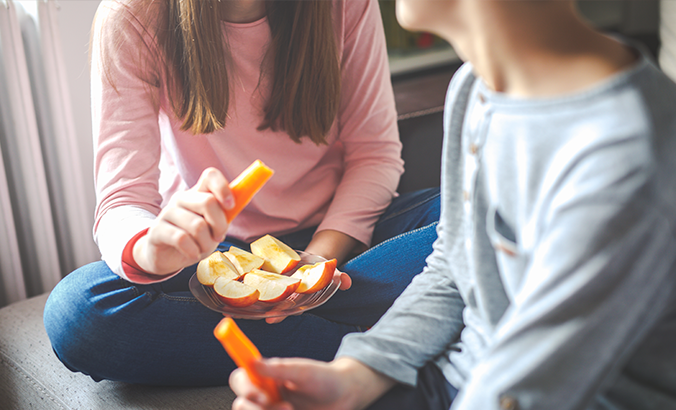 Kinder essen gemeinsam Möhren und Apfelspalten