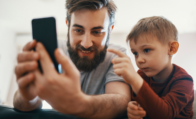 Vater schaut gemeinsam mit Sohn auf ein Smartphone