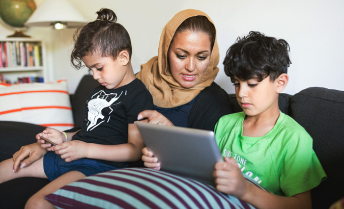 Mutter schaut gemeinsam mit Kindern auf Tablet und Smartphone