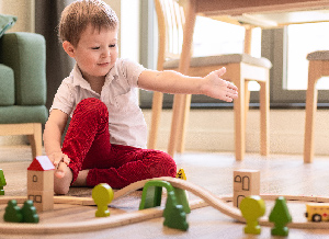 Ein Kind spielt mit einer Eisenbahn aus Holz und zeigt mit seinem Arm auf die gebaute Strecke.