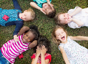 Sechs Kinder liegen in einem Kreis auf einer Wiese und sind dabei sichtlich erfreut über etwas.