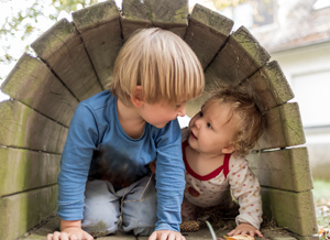 Zwei Kinder spielen miteinander in einem Holztunnel