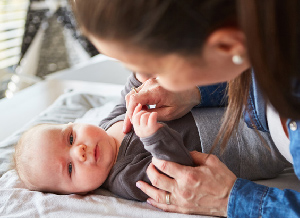 Eine Mutter spielt mit ihrem Baby, nachdem es dieses auf einem Wickeltisch frisch gewickelt hat.