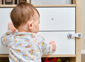 Kleinkind und ein Holzschrank mit Kindersicherung