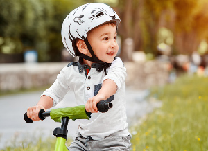 Ein Kind sitzt auf einem Lauffahrrad und überquert dabei einen Spielplatz.