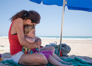 Mutter hält ihr Kind am Strand unter einem Sonnenschirm im Arm