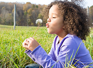 Mädchen bläst gegen Pusteblume