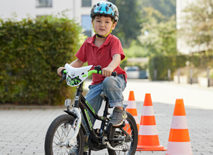 Junge fährt mit Helm auf einem Fahrrad um Slalom-Kegel 
