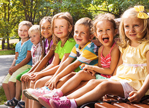 Kinder sitzen draußen im Grünen in einer Reihe